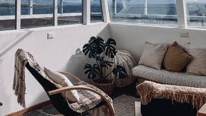 Une pièce avec de grandes fenêtres, un canapé, un fauteuil et une plante en pot.