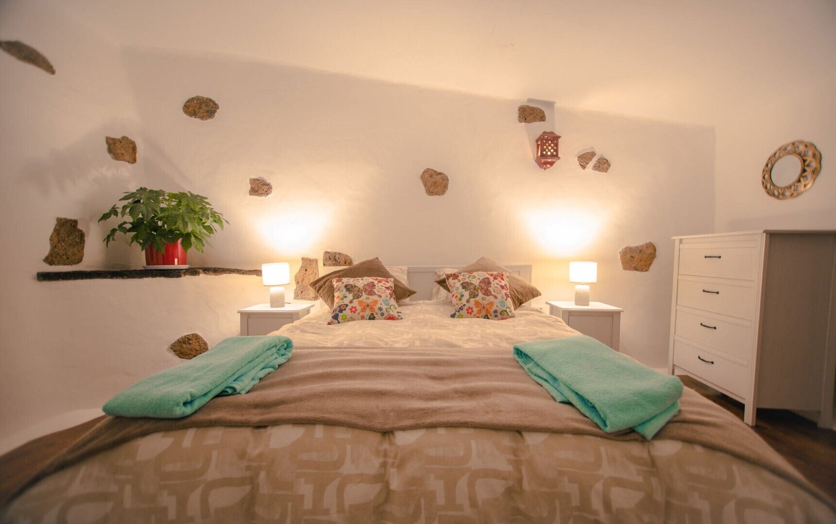 A bedroom with a bed, two bedside tables with lamps, a dresser, and decorative rocks on the walls.