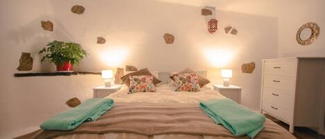 A bedroom with a bed, two bedside tables with lamps, a dresser, and decorative rocks on the walls.