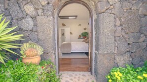 Un arco in pietra conduce a una camera da letto con un letto, un comodino e una pianta in vaso.