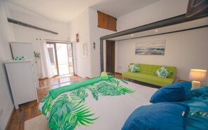 A bedroom with a bed, a green sofa, a white cabinet, and a painting on the wall.