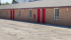 Un edificio largo de ladrillo con puertas y ventanas rojas, un estacionamiento al frente y un cielo despejado.