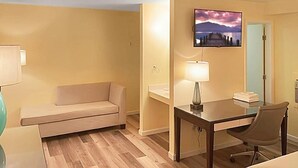 Habitación de hotel con sofá, escritorio, silla, televisor montado en la pared y cama.