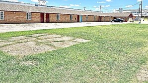 Una hilera de edificios de ladrillo de una sola planta con techo plano, un área verde al frente y un cielo azul despejado.