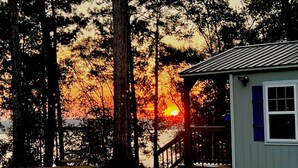 Eine Hütte mit Veranda, die auf einen Wald und einen Sonnenuntergang blickt.