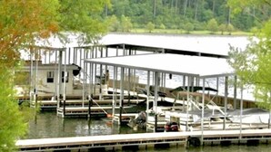 Ein an einem Ufer vertäutes Boot mit einem überdachten Bereich, umgeben von Bäumen und Wasser.