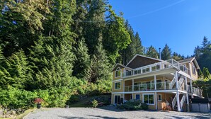 A multi-story lodge with a gravel driveway and dense forest backdrop. - Comfortable one bedroom by the ocean (Cowichan Bay)