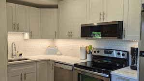 A modern kitchen with stainless steel appliances, white cabinetry, and a wooden floor. - Comfortable one bedroom by the ocean (Cowichan Bay)