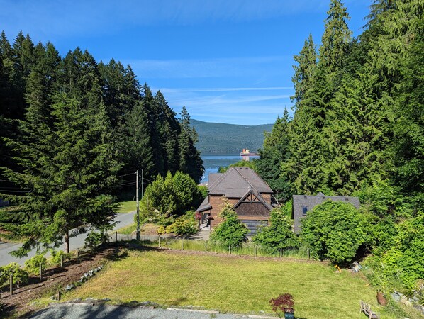 Un quartier résidentiel avec une maison entourée d’une forêt dense, une vue dégagée sur un lac et un navire visible au loin sur l’eau.
