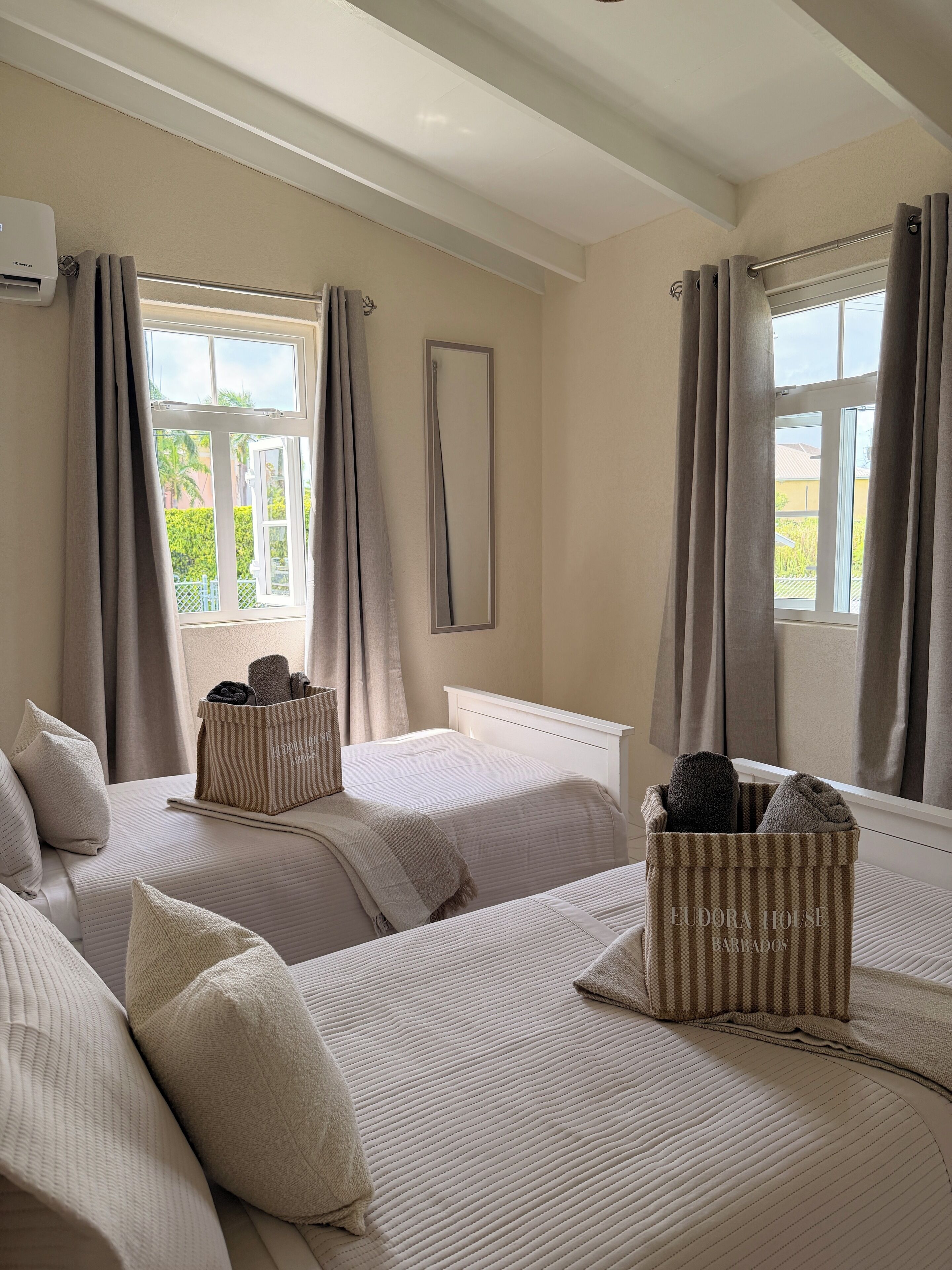 A hotel room with two beds, a large window, a radiator, and a mirror.