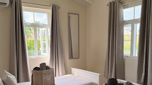 Habitación de hotel con dos camas, ropa de cama color beige, un espejo grande y una ventana con cortinas.