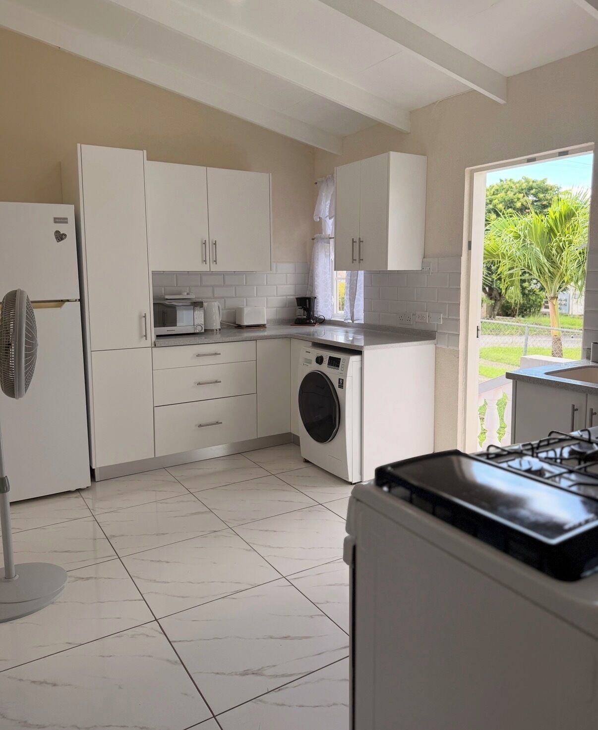 A modern kitchen with white cabinets, a built-in washing machine, a gas stove, and a large window offering a view of greenery outside.