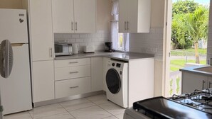 Cocina moderna con armarios blancos, lavadora integrada, cocina a gas y un amplio ventanal con vistas al exterior.