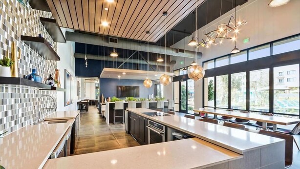 Een moderne keuken met een centraal kookeiland, hanglampen en grote ramen met uitzicht op de omgeving.