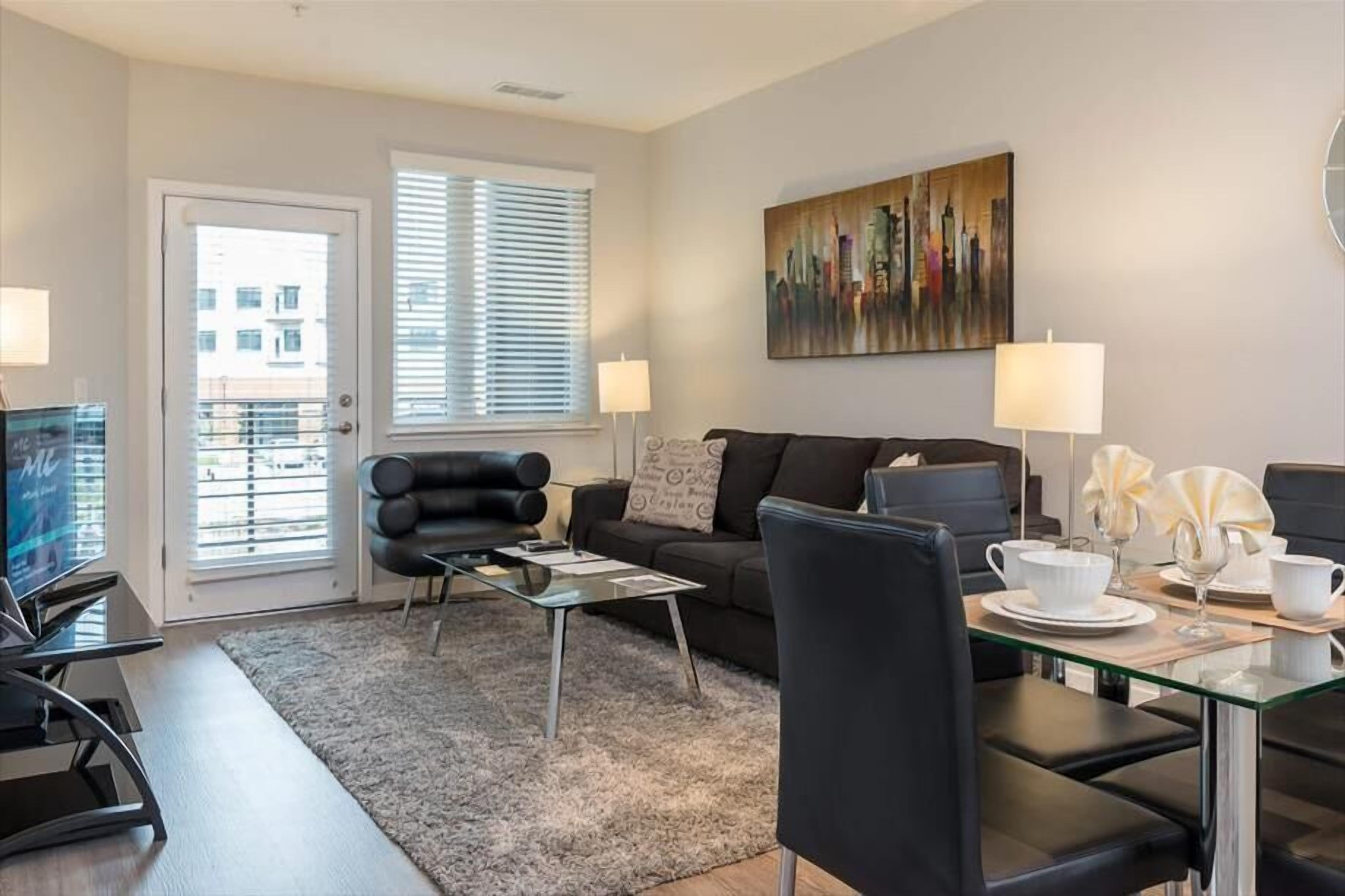 Een moderne woonkamer met een bank, een glazen salontafel, een televisie en een schilderij aan de muur.