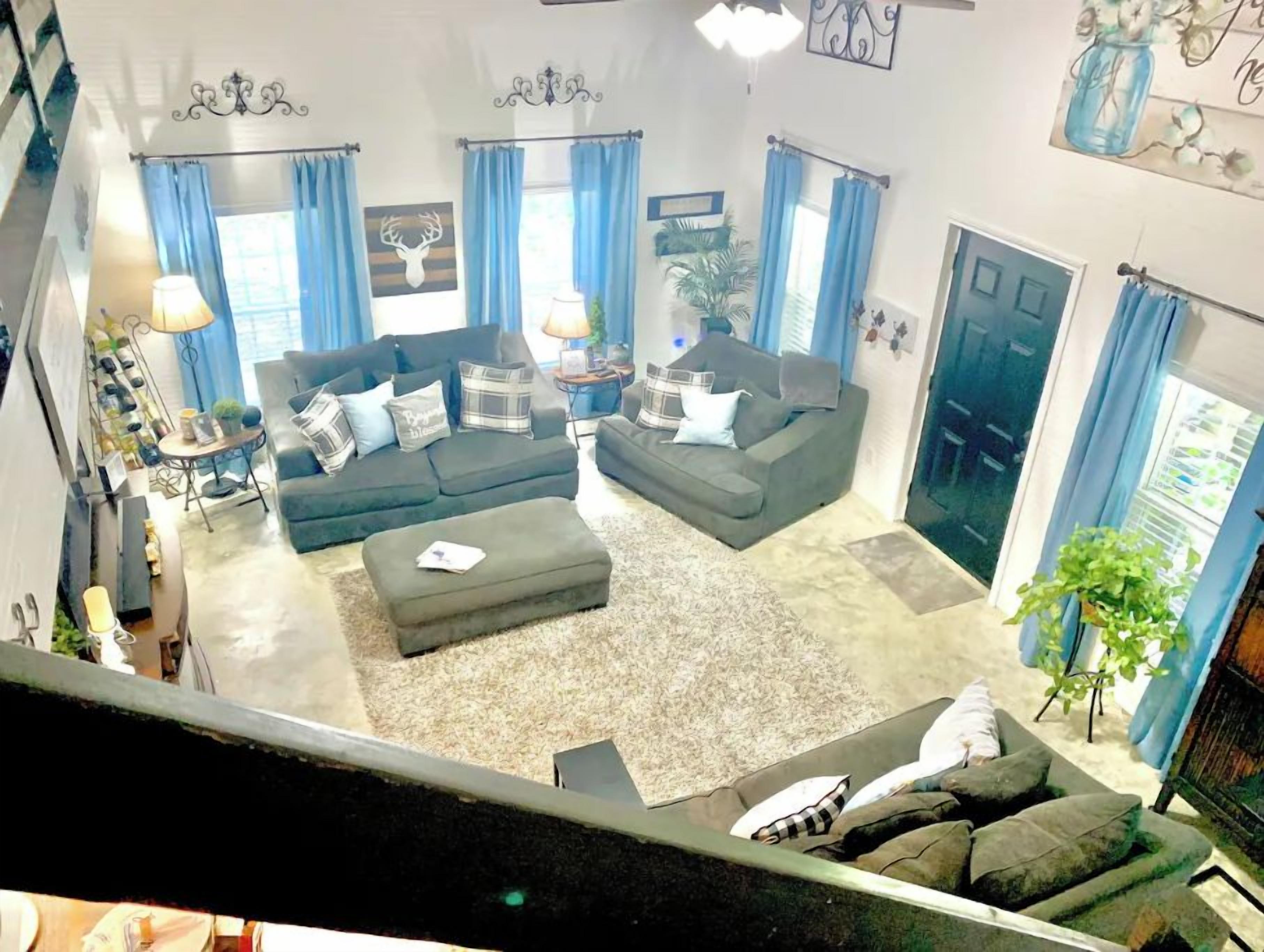 A living room with a sectional sofa, a coffee table, and a small side table. There are blue curtains, a chandelier, and a plant.