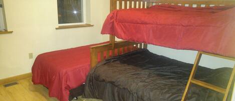 Una habitación pequeña con una cama individual y una literas de madera, y una colcha roja.
