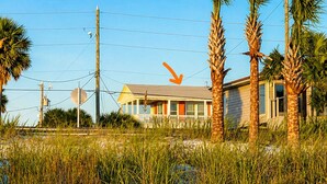 A beach with a wooden fence, palm trees, and a house in the background. - Clown Fish Cottage - Pet Friendly with King Bed (Mexico Beach)