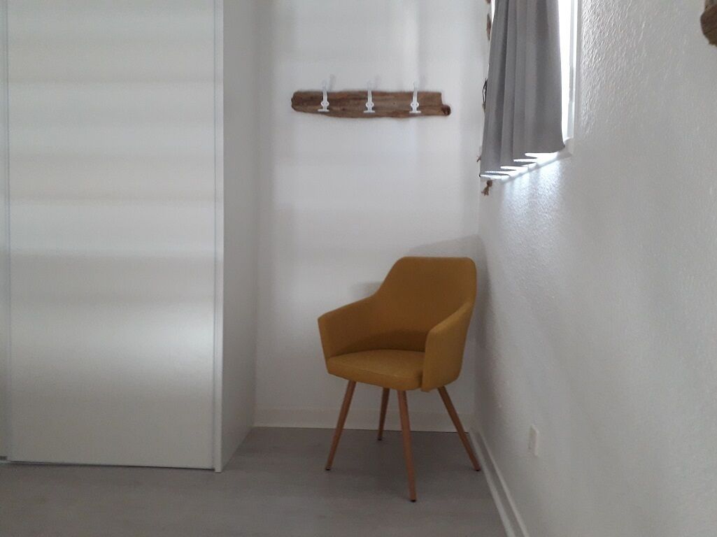 Ett rum med en enda senapsgul stol, en vit dörr, en trähylla med ljus och ett fönster med gardiner.