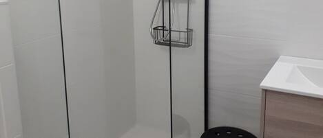 A modern bathroom with a glass-enclosed shower, a toilet, a sink, and a small stool.