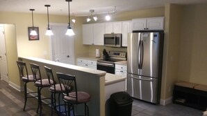 A kitchen with a central island, bar stools, stainless steel appliances, and pendant lighting. - Spacious Downtown, First Floor, Patio, sleeps up to 6, Short Walk to Everything! (Traverse City)