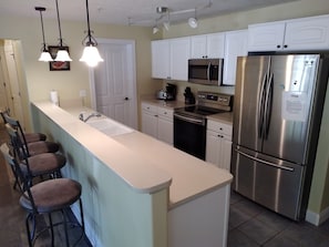 A kitchen with a central island, stainless steel appliances, white cabinets, and pendant lighting. - Spacious Downtown, First Floor, Patio, sleeps up to 6, Short Walk to Everything! (Traverse City)