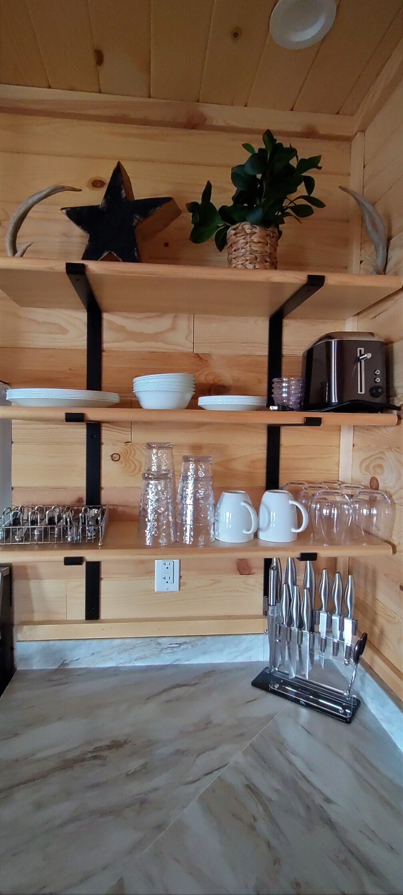 A wooden interior with shelves holding kitchenware, a toaster, and a plant.
