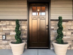 A brown door with a glass panel and a small window above it, flanked by two large potted plants.