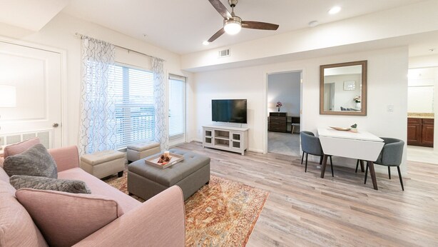 Uma sala de estar moderna com um sofá, um banquinho e uma TV. Há uma área de jantar com mesa e cadeiras.