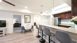 Cozinha moderna com bancada, piso de madeira e área de refeições com televisão e cadeiras.