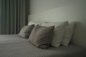 A bed with a herringbone-patterned bedspread and two pillows, one with a chevron pattern and the other plain.