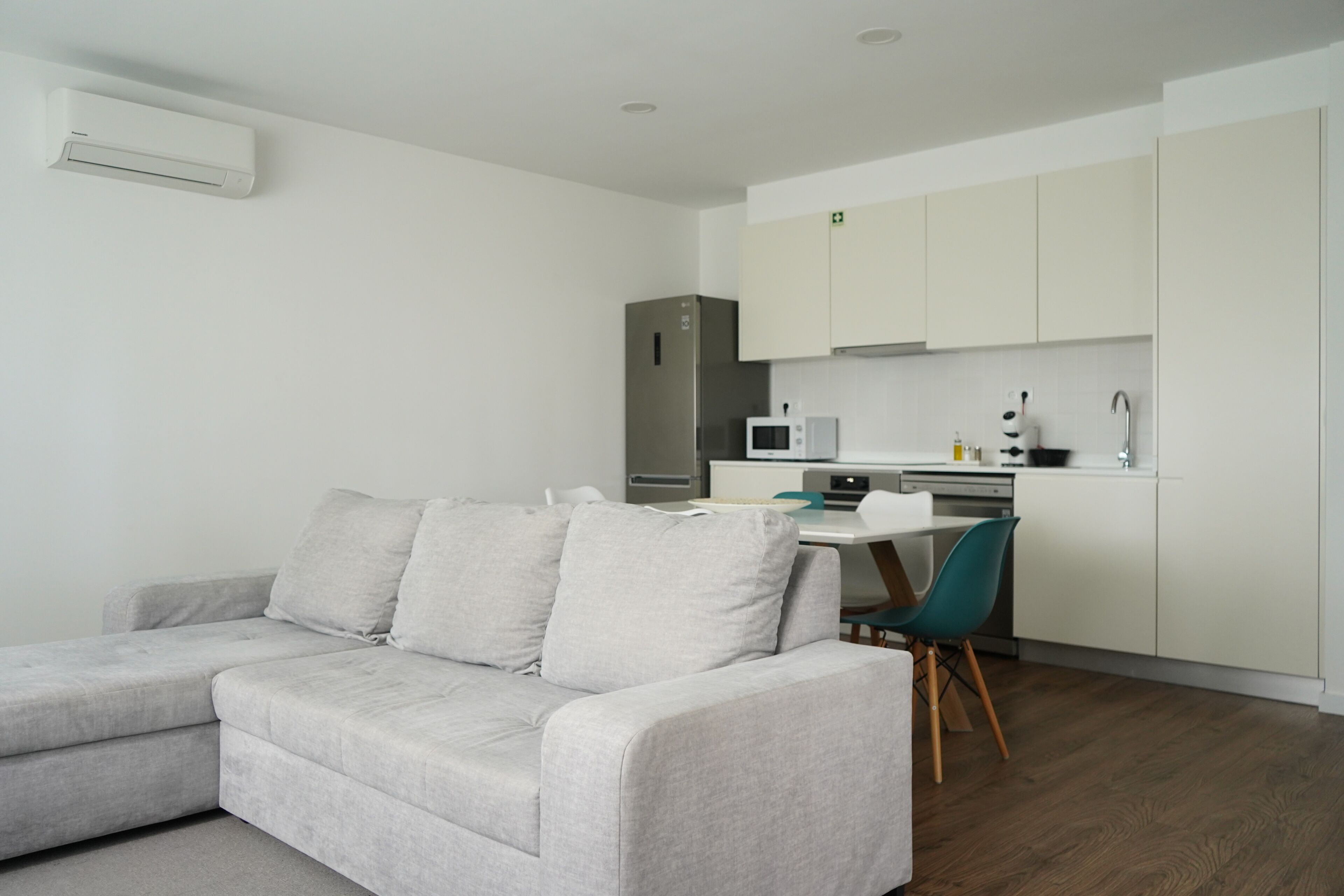 A modern living room with a grey sofa and a dining area with a white table and chairs.