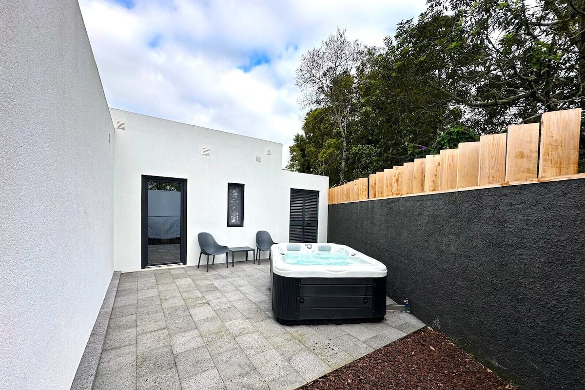 Un patio moderno al aire libre con un jacuzzi, dos sillas y una valla de madera.