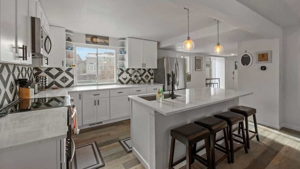 A modern kitchen with white cabinets, a large island with stools, pendant lighting, and a view of the city.