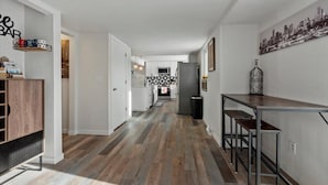A modern kitchen with a patterned backsplash, a dining area with metal stools, and a hallway with wooden flooring.