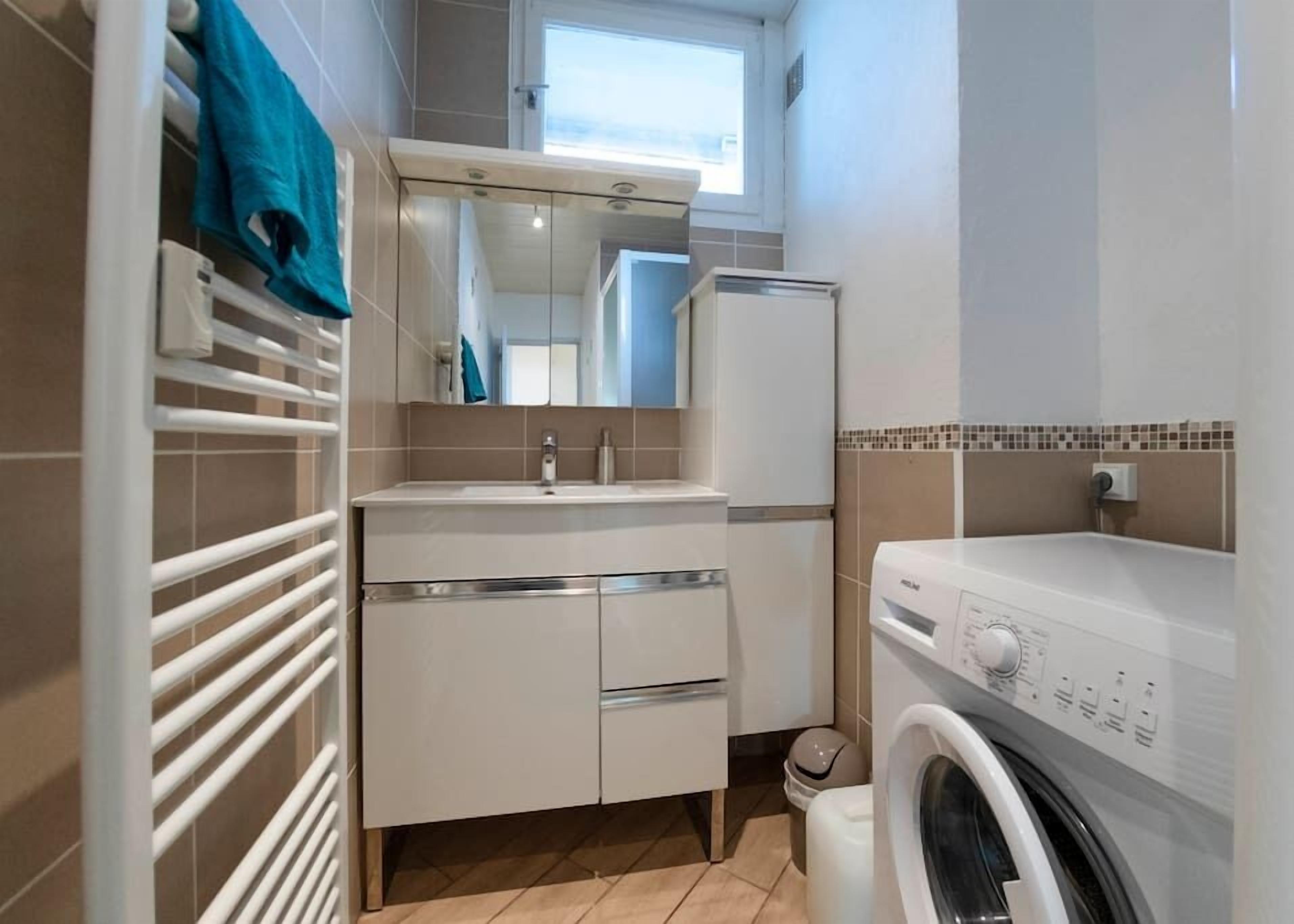A compact bathroom with a white sink, mirror, and a washing machine.