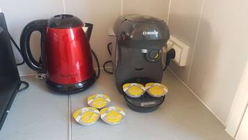 A kitchen with a red electric kettle and a black coffee maker, both connected to power outlets. There are four yellow containers with lids on the counter.