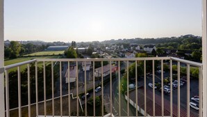A balcony with a view of a residential area, including houses, a parking lot, and a green field. - Appart'Hôtel L'ile en Mouvement (Montbéliard)