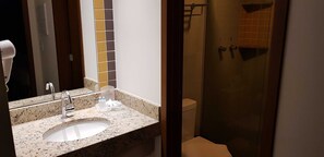 Bathroom features a granite countertop, white sink, handheld hair dryer, glass shower enclosure, and a tiled floor.