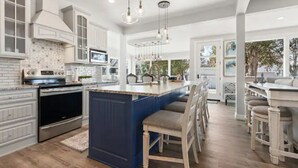 Uma cozinha espaçosa com armários brancos, uma ilha azul e uma grande janela com vista para um jardim.