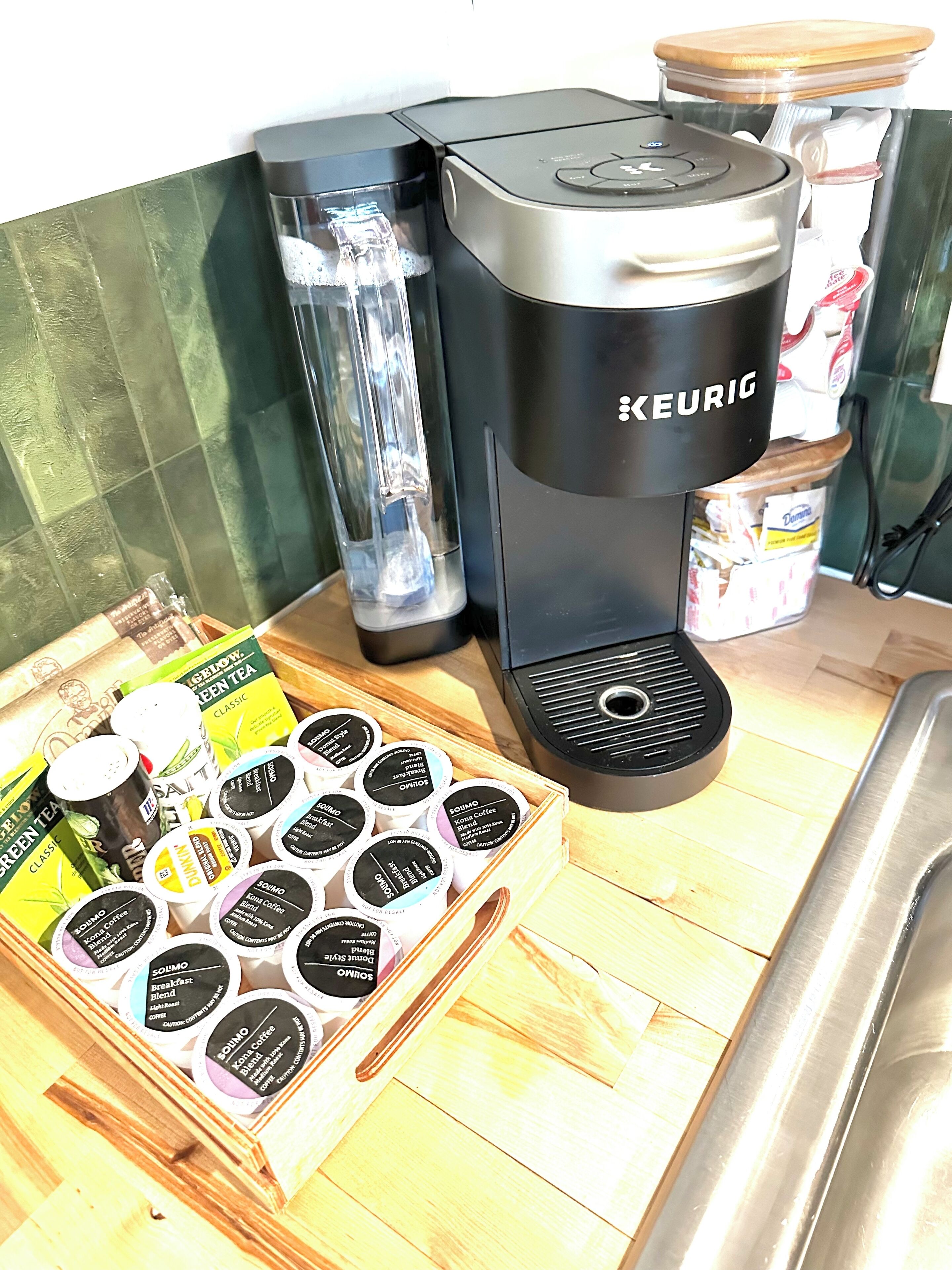 A kitchen with a Keurig coffee maker, a blender, and a wooden tray with coffee pods.