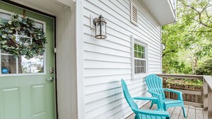 Een veranda met twee turquoise Adirondack-stoelen, een groene deur en een witte buitenmuur.