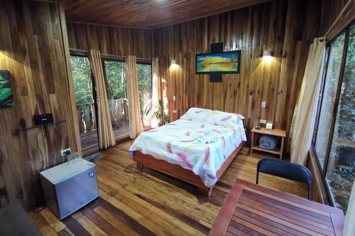 A wooden cabin room with a bed, a TV, a small table, and a refrigerator.