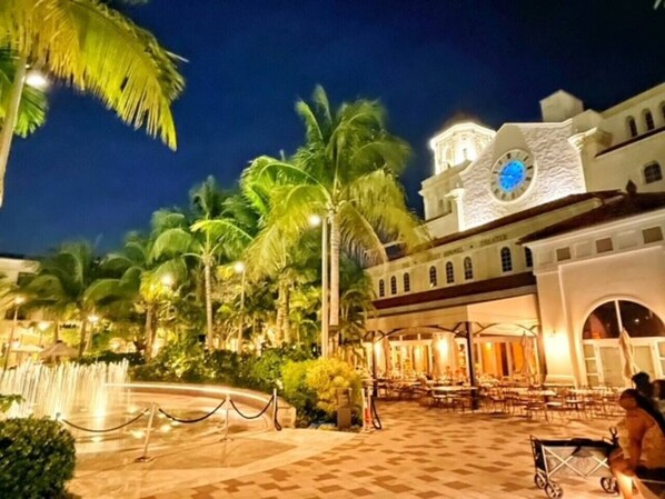 A hotel courtyard with palm trees, a fountain, and outdoor seating.