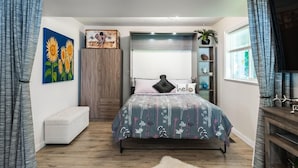 A bedroom with a bed, a bench, a wall with a painting, a shelf with decorative items, and a window with curtains. - Nesting Ravens B@B .Large ,  suite on Private Acreage, Safe and enjoyable stay! (Nanaimo)
