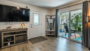 A living room with a flat-screen TV, wooden entertainment unit, and a sliding glass door leading to an outdoor patio. - Nesting Ravens B@B .Large ,  suite on Private Acreage, Safe and enjoyable stay! (Nanaimo)