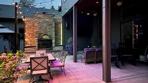 Een terras buiten met een stenen open haard, sfeerverlichting en tuinmeubels.
