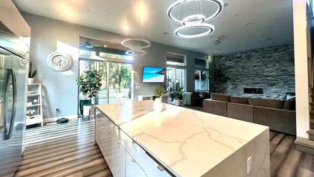 Een moderne keuken met een marmeren aanrechtblad, hanglampen en een wand bekled met natuursteen.