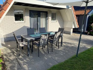 An outdoor patio with a table and chairs, a window with curtains, and a brick wall.