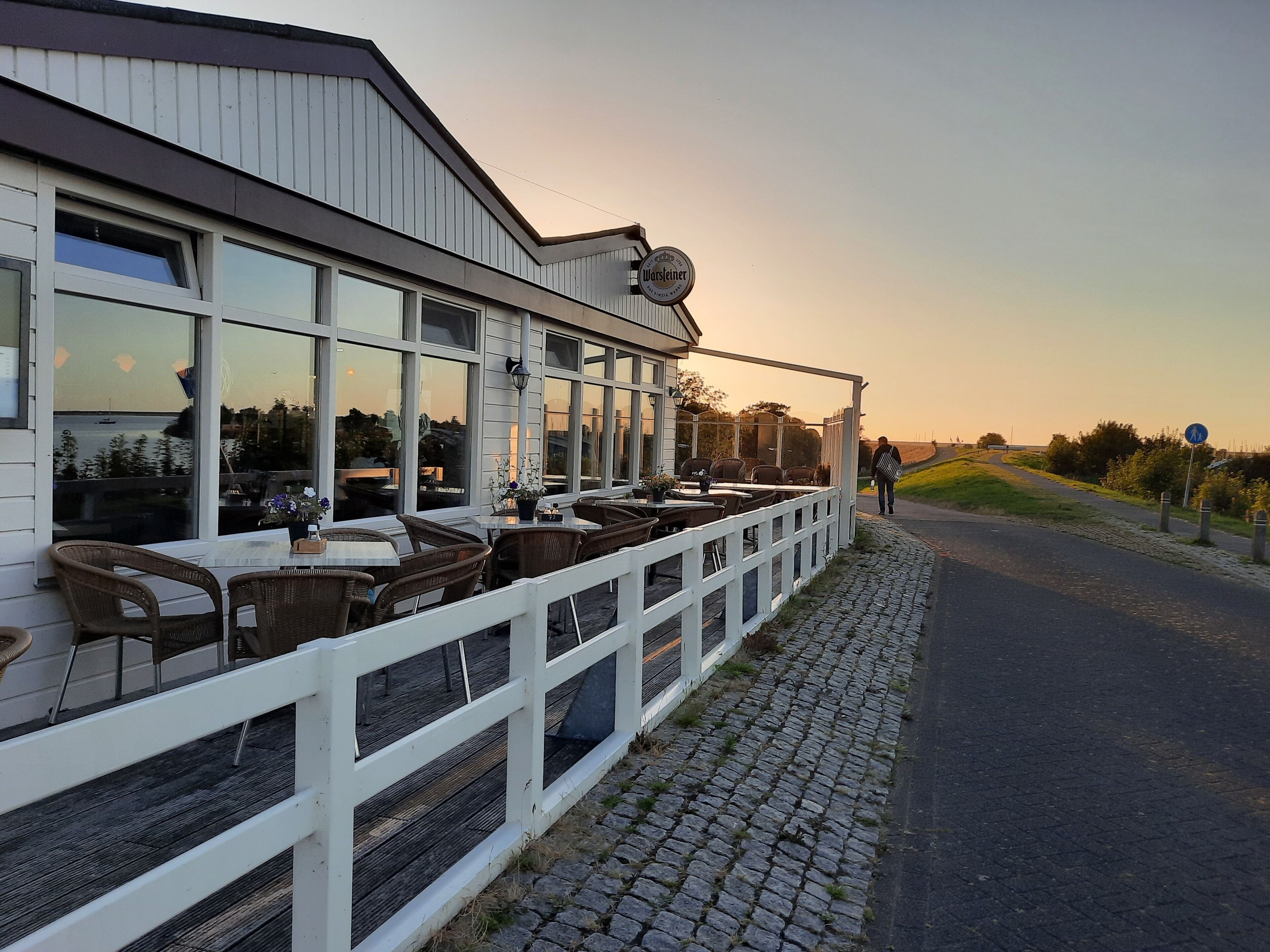 Een restaurant met terras, een witte omheining en een geplaveid pad.